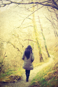 A  girl walking on the path  leading into the woods